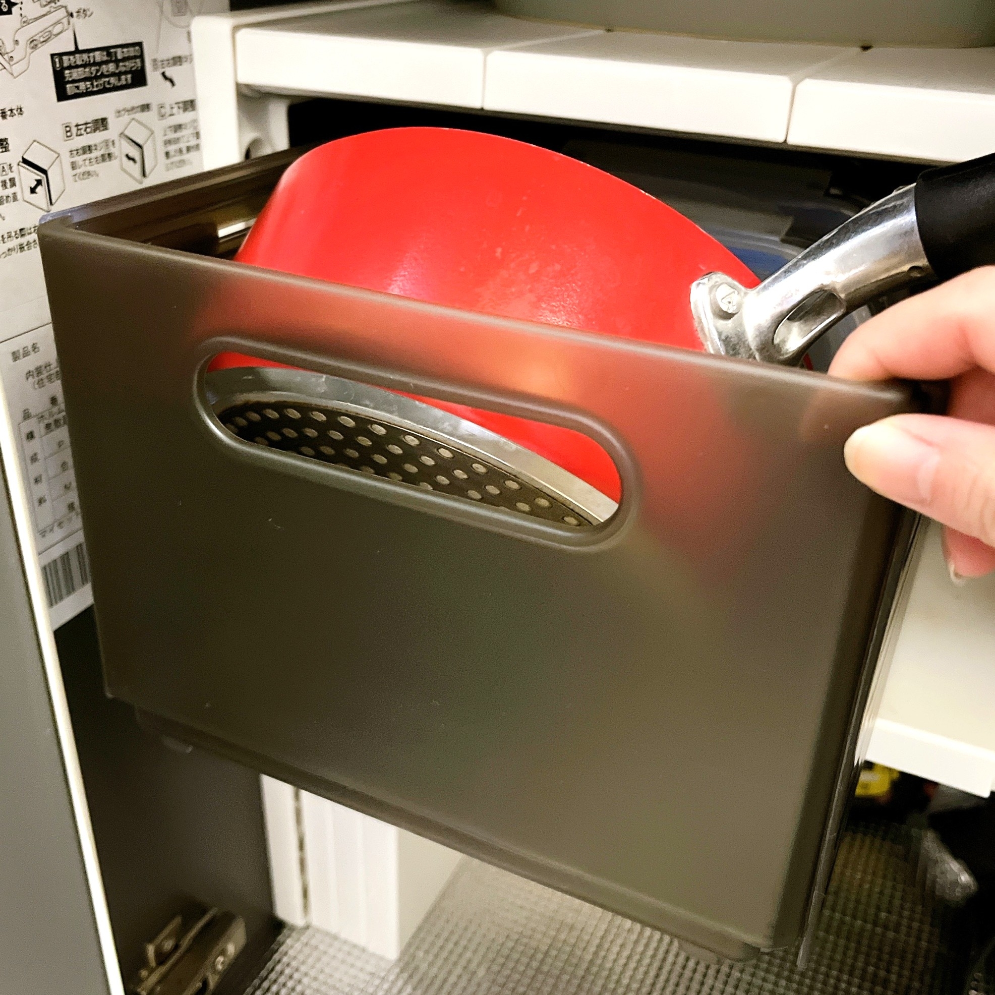 キッチンの下の収納キャビネットから取っ手のついた鍋を取り出す手。