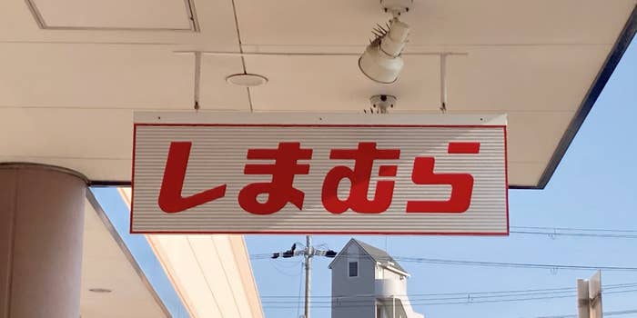 A store sign with Japanese text "しまむら" hangs outside a building