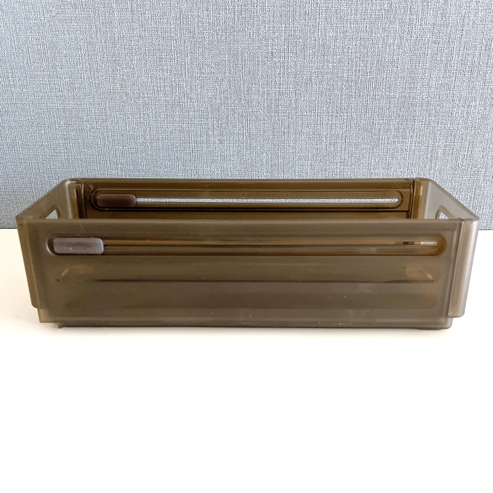 茶色のプラスチック製収納ボックスがテーブルに置かれています。背景にファブリック素材の壁があります。