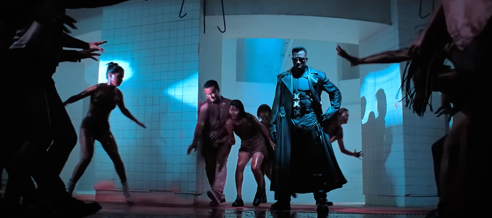 Blade stands amongst frenzied people covered in blood, wearing sunglasses and a trenchcoat