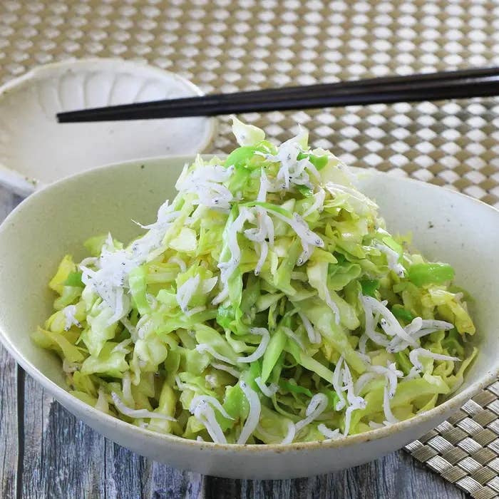 ボウルに盛られたキャベツと白い小魚のサラダ。背景に箸と小さな皿が置かれている。