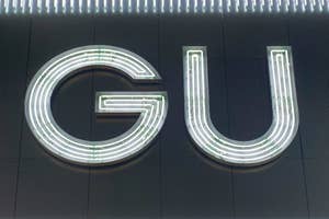 Large lit-up letters "GU" on a dark wall, against striped illumination above