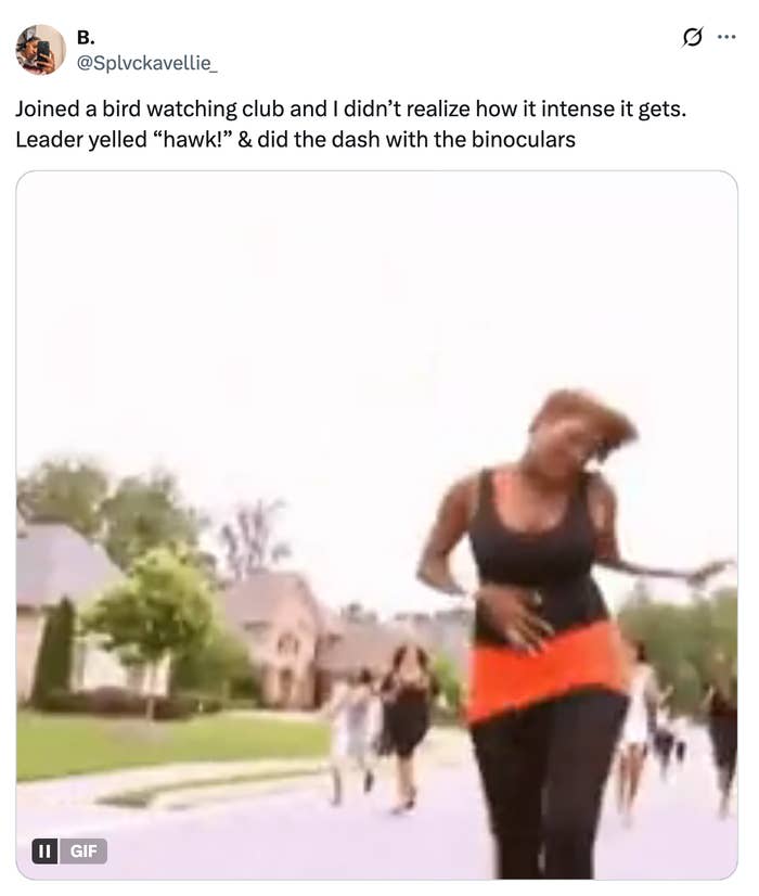 A person runs down a street with a binoculars in a humorous bird-watching moment. Others are seen in the background