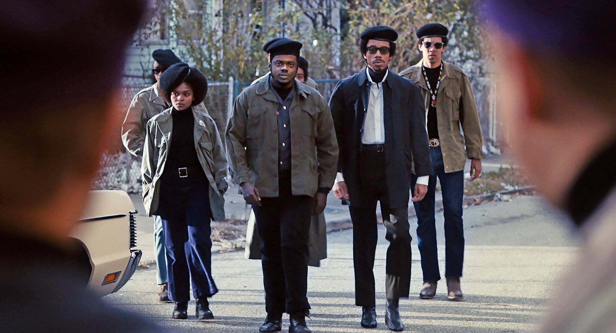 Group dressed in 1960s revolutionary style, including berets and jackets, walking on a street