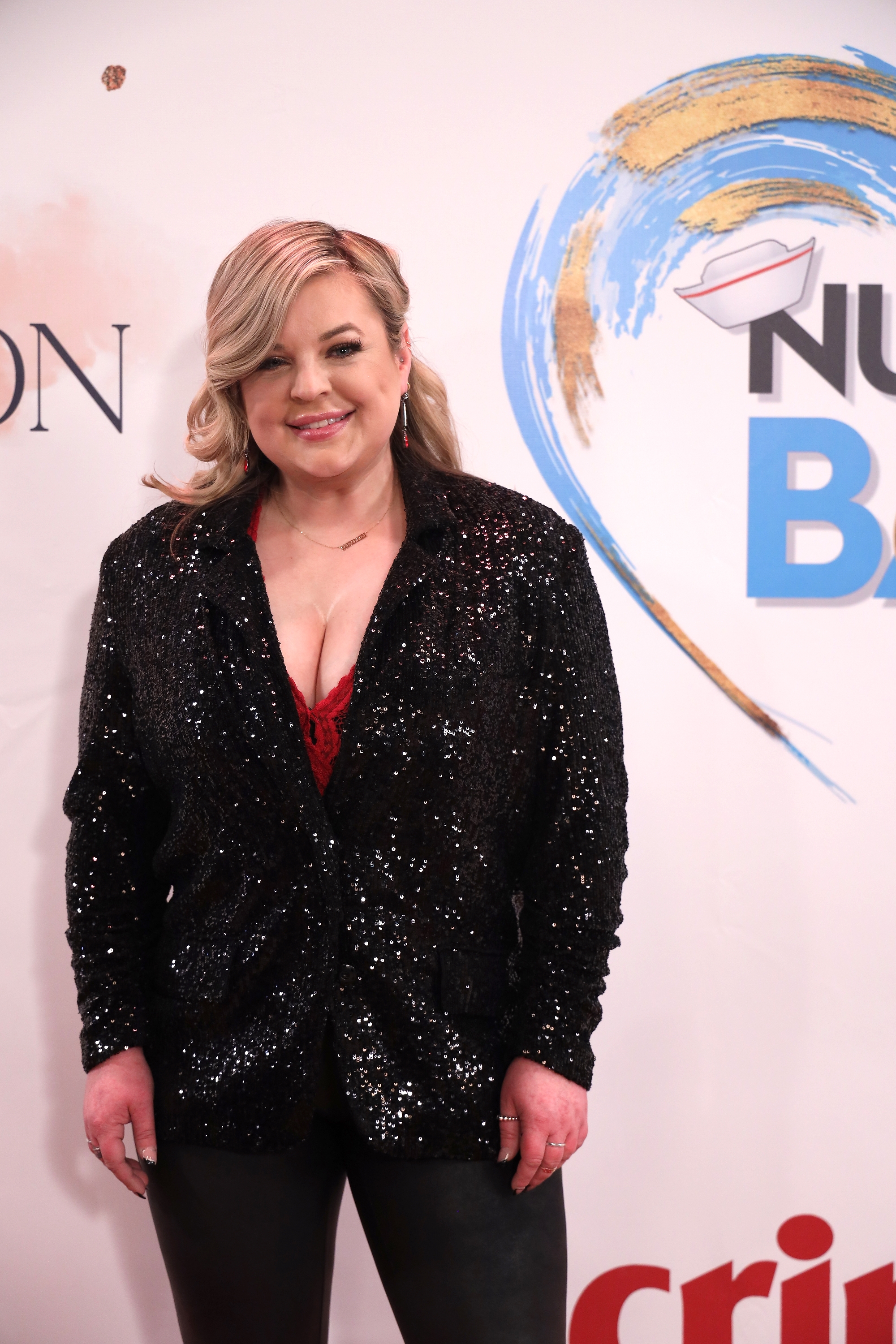 Person in a sequined blazer and red top poses on the red carpet at an event
