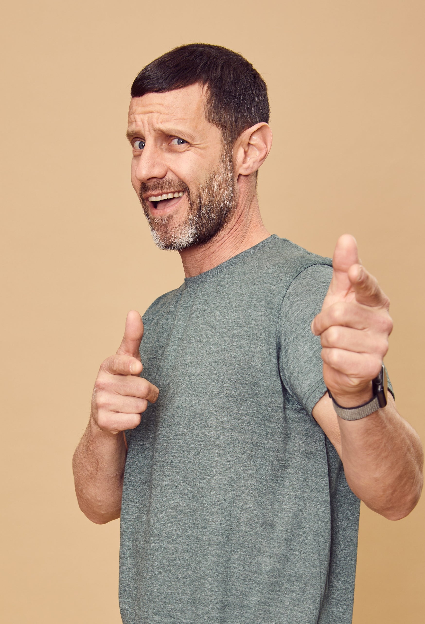 Person in a casual outfit, grey t-shirt and pants, pointing playfully and smiling against a plain background