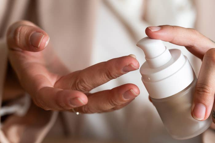 Person applying skincare product with a pump bottle, focusing on fingers and product application