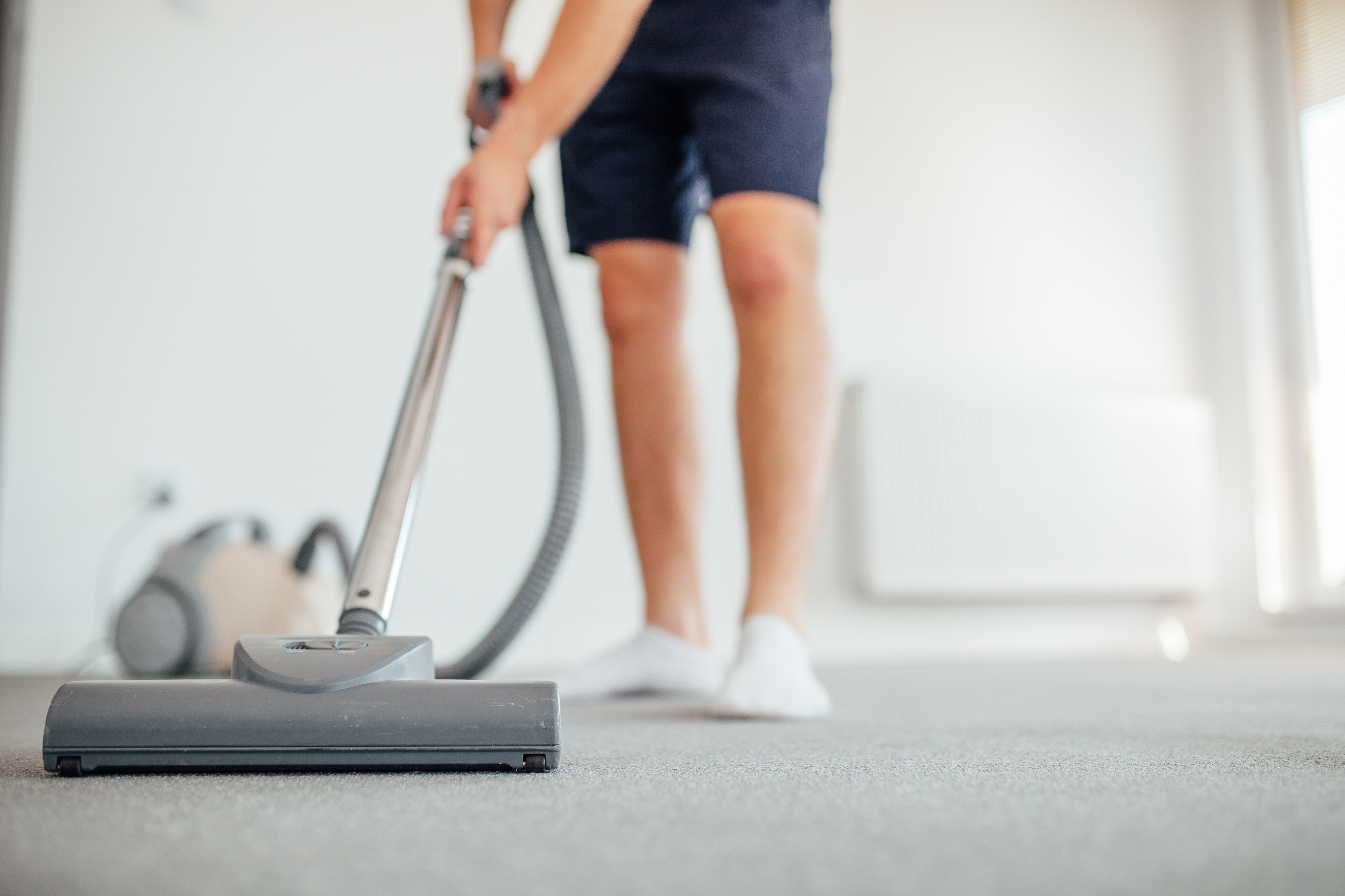 Person using a vacuum cleaner on a carpeted floor indoors, focusing on the cleaner’s head