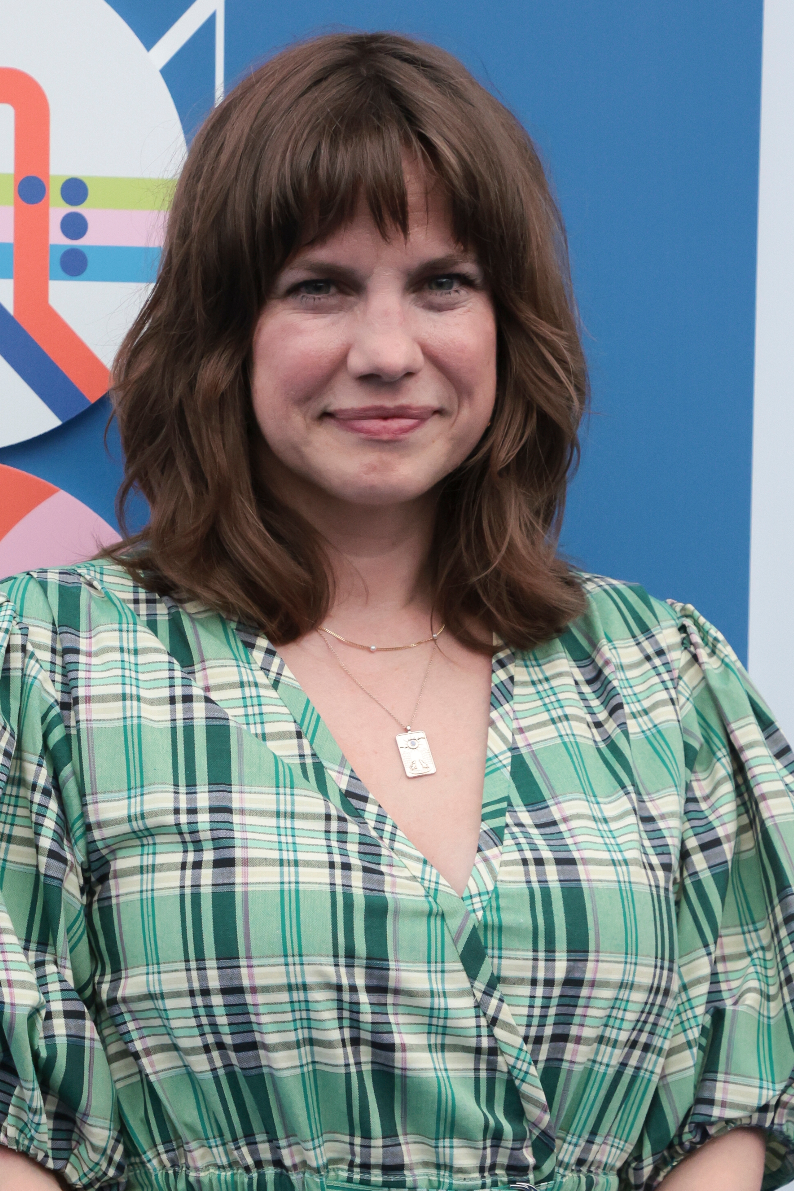 Person in plaid dress at an event, smiling with shoulder-length hair