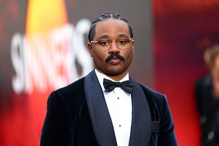 Person in formal attire with braids and glasses, wearing a velvet tuxedo, at a red carpet event