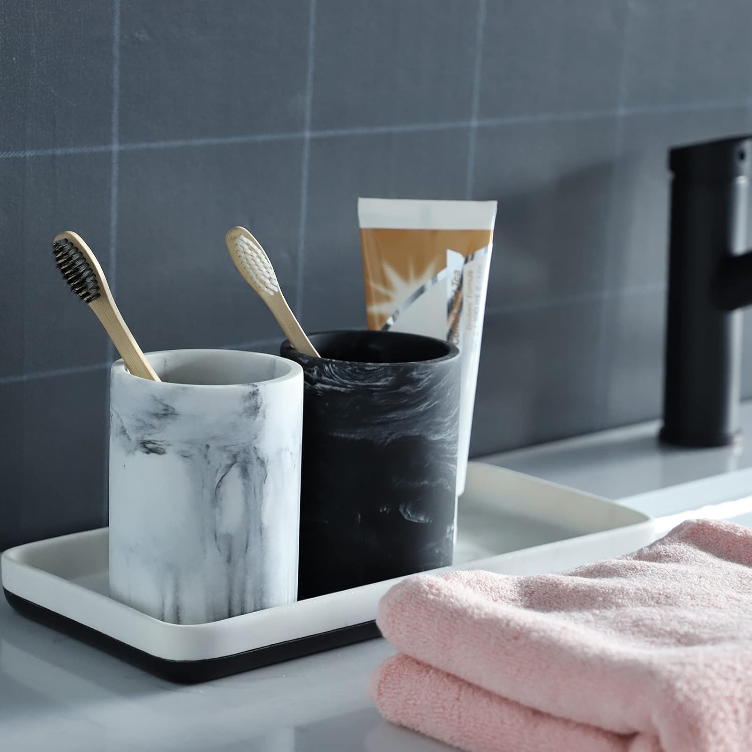 Bathroom counter with two toothbrushes in marble holders, toothpaste, and a pink towel on a tray, suggesting luxury bathroom accessories