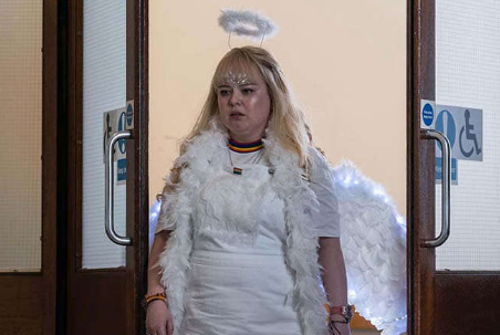 Claire from "Derry Girls" dressed as an angel in a white outfit with feathered wings and a halo, looking upset