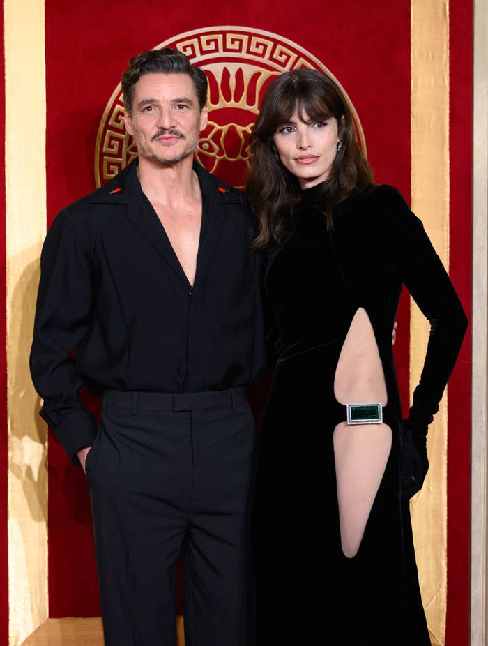 Pedro and Lux Pascal on a red carpet; one in a deep V-neck black shirt, the other in a long-sleeve black dress with a cutout