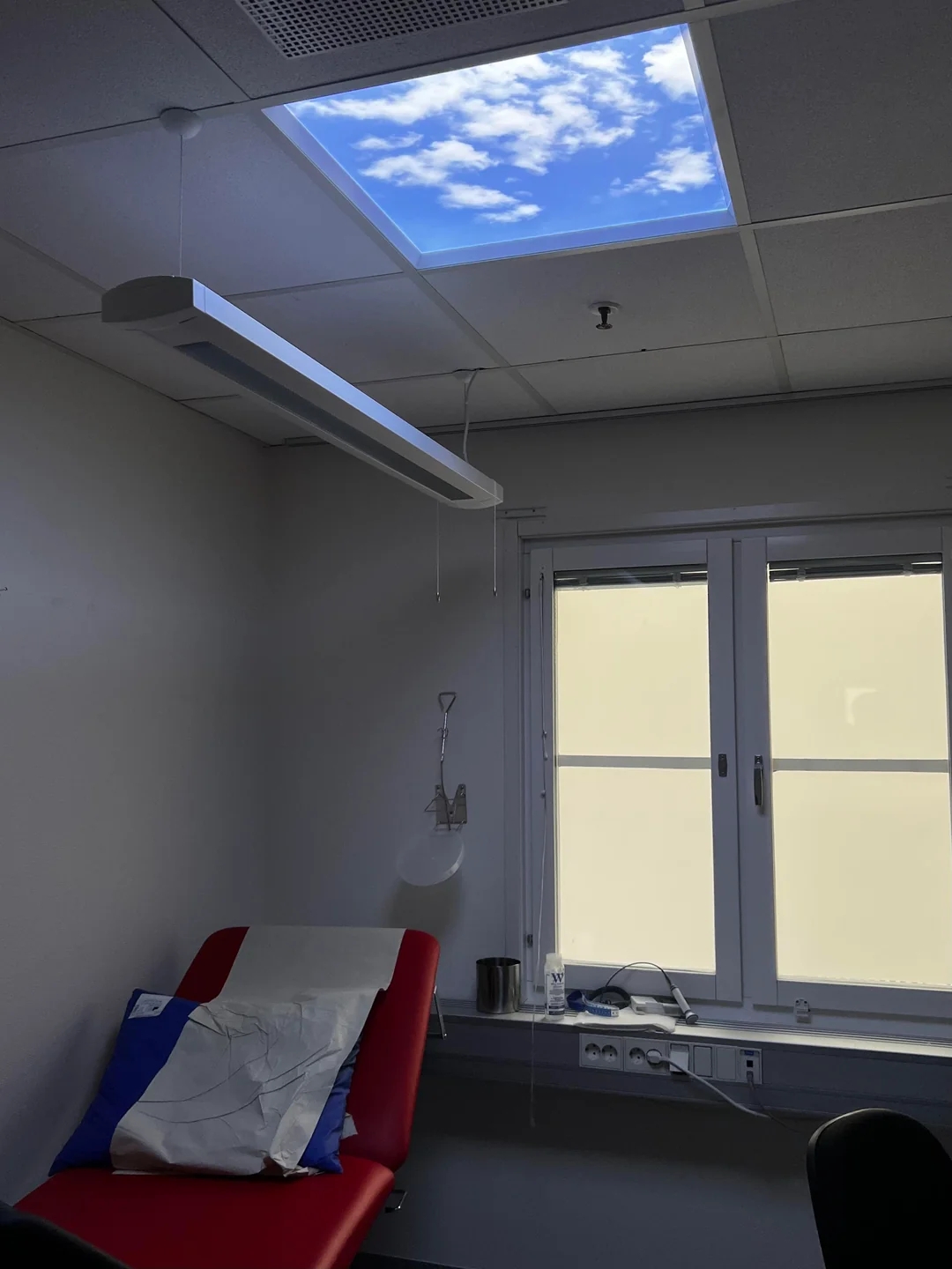Ceiling light with a sky and cloud design in a room with a chair and a window