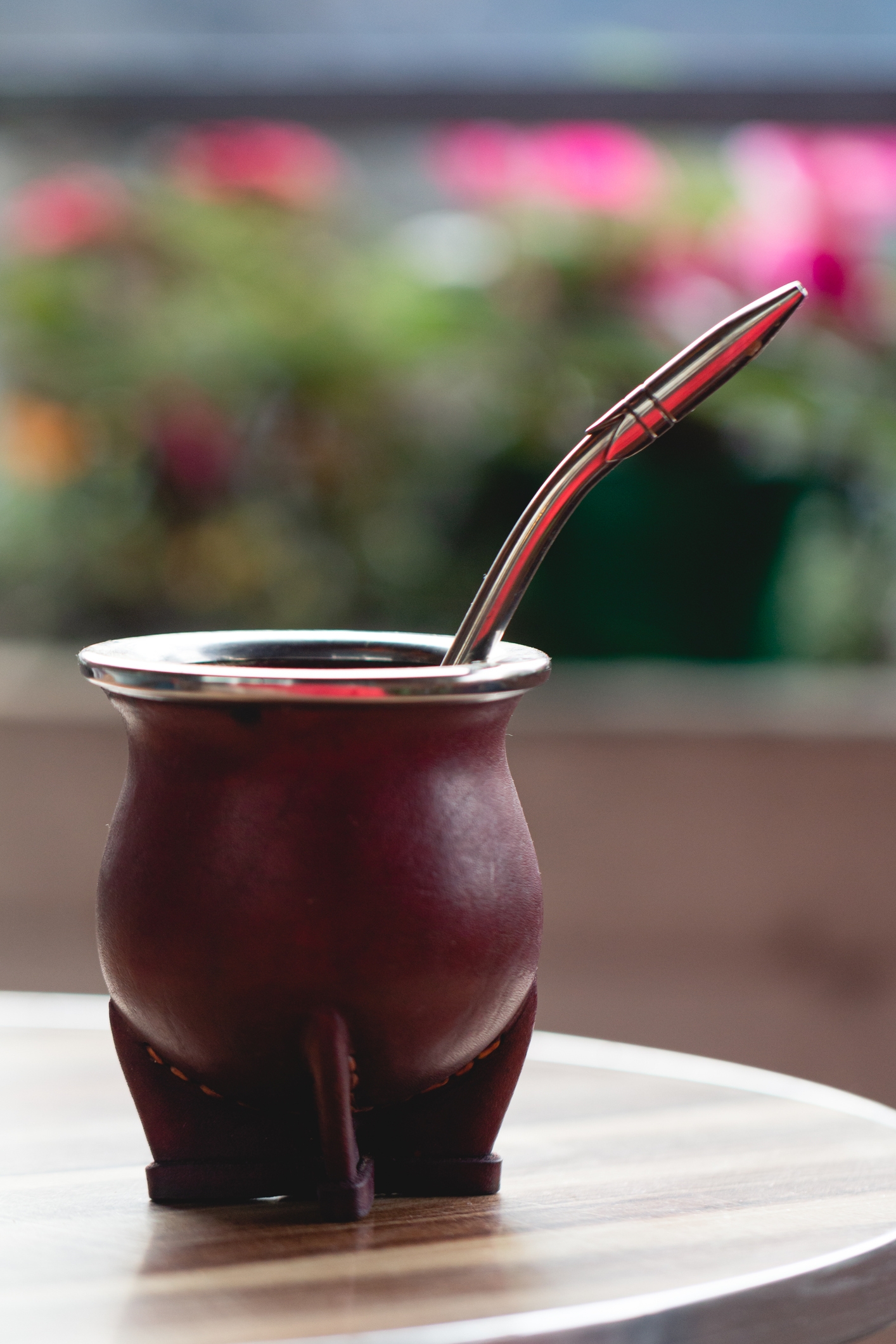 A traditional mate gourd with a metal straw on a table, set against a blurred background with flowers