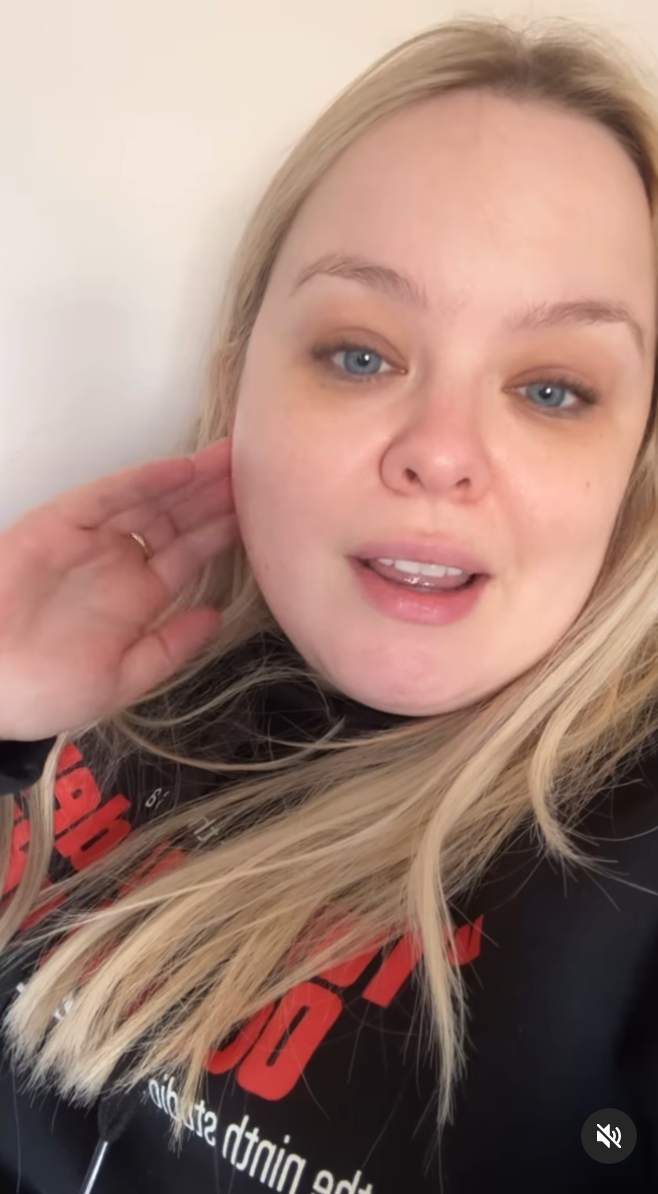 Nicola Coughlan with long hair, speaking directly to camera, wears a casual black sweatshirt with text