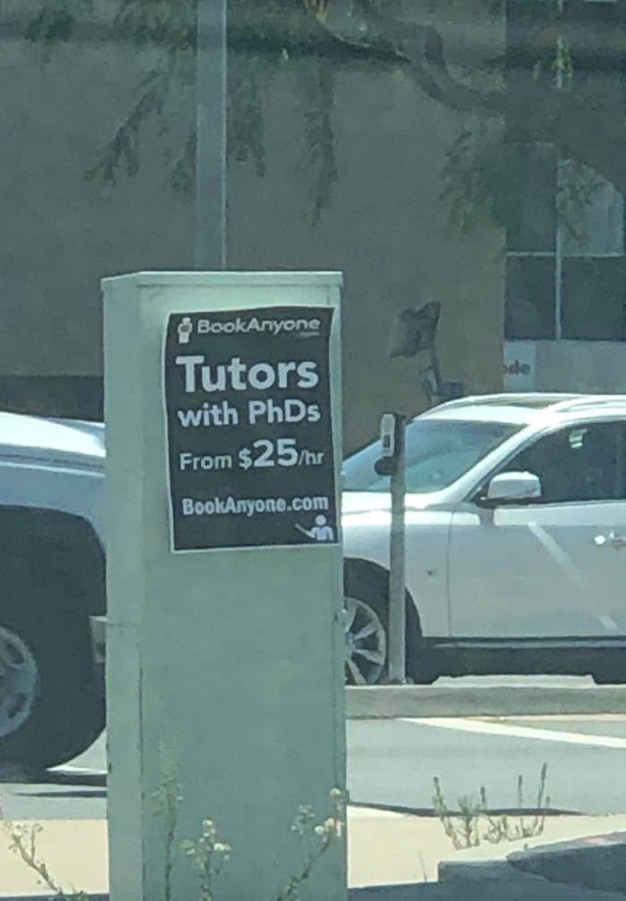 Sign advertising PhD tutors from $25/hr at BookAnyone.com, displayed on a pole near parked cars