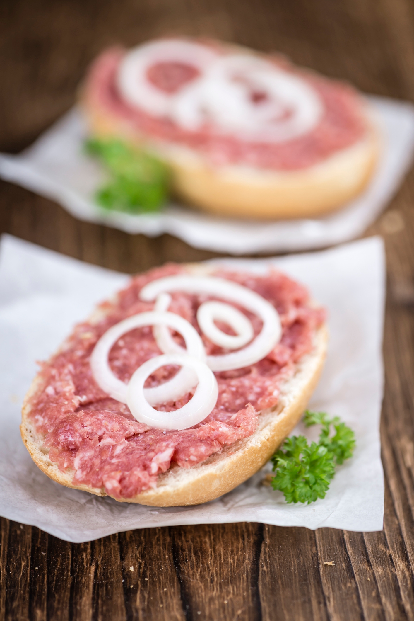 Bread roll topped with raw ground meat and onion rings, garnished with parsley