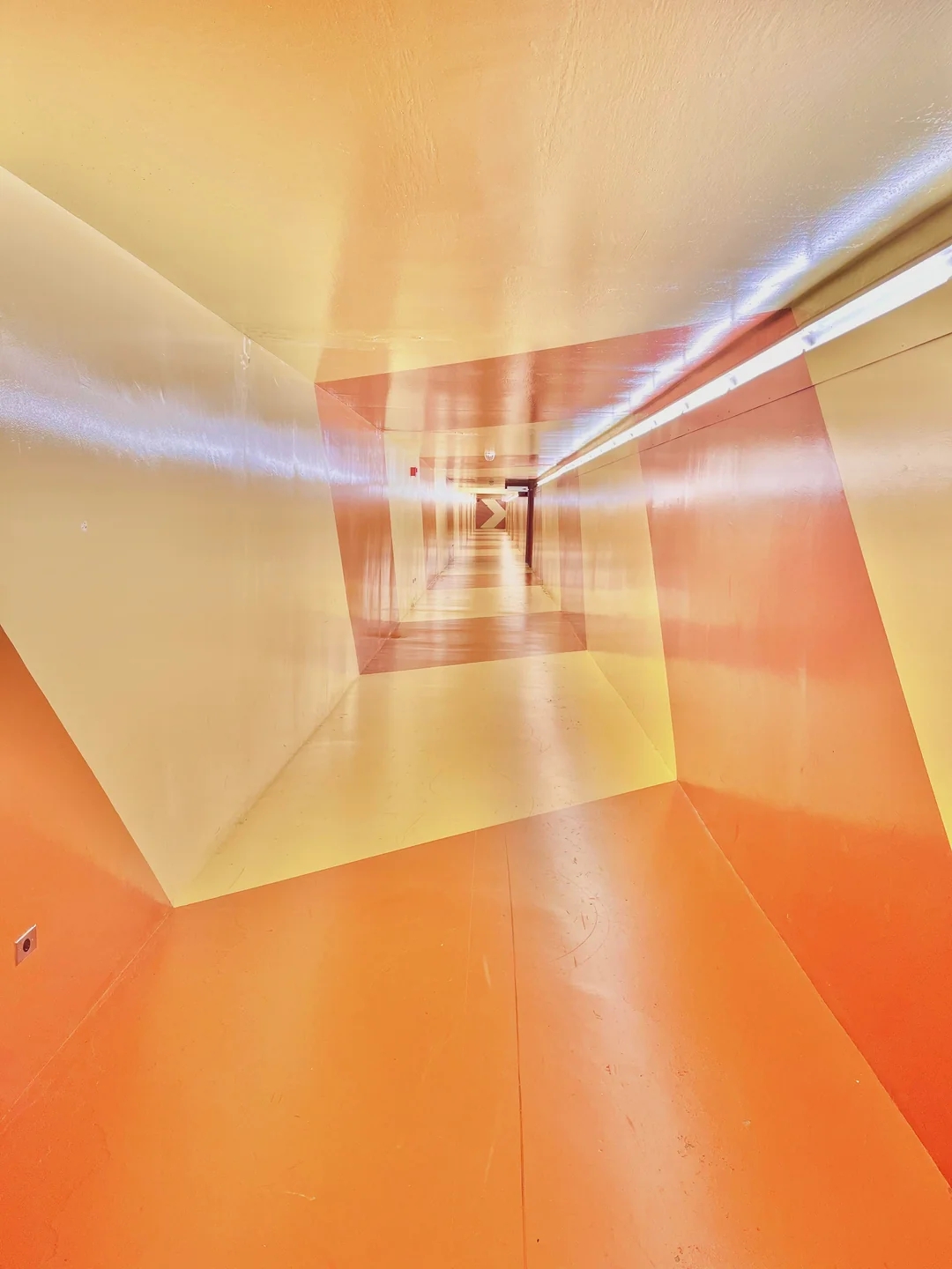 A skewed, geometric hallway with walls and ceilings in contrasting colors, giving an optical illusion effect