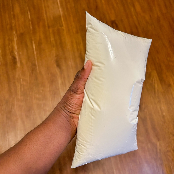 A hand holding a filled, sealed plastic bag, likely containing a liquid, against a wooden floor background