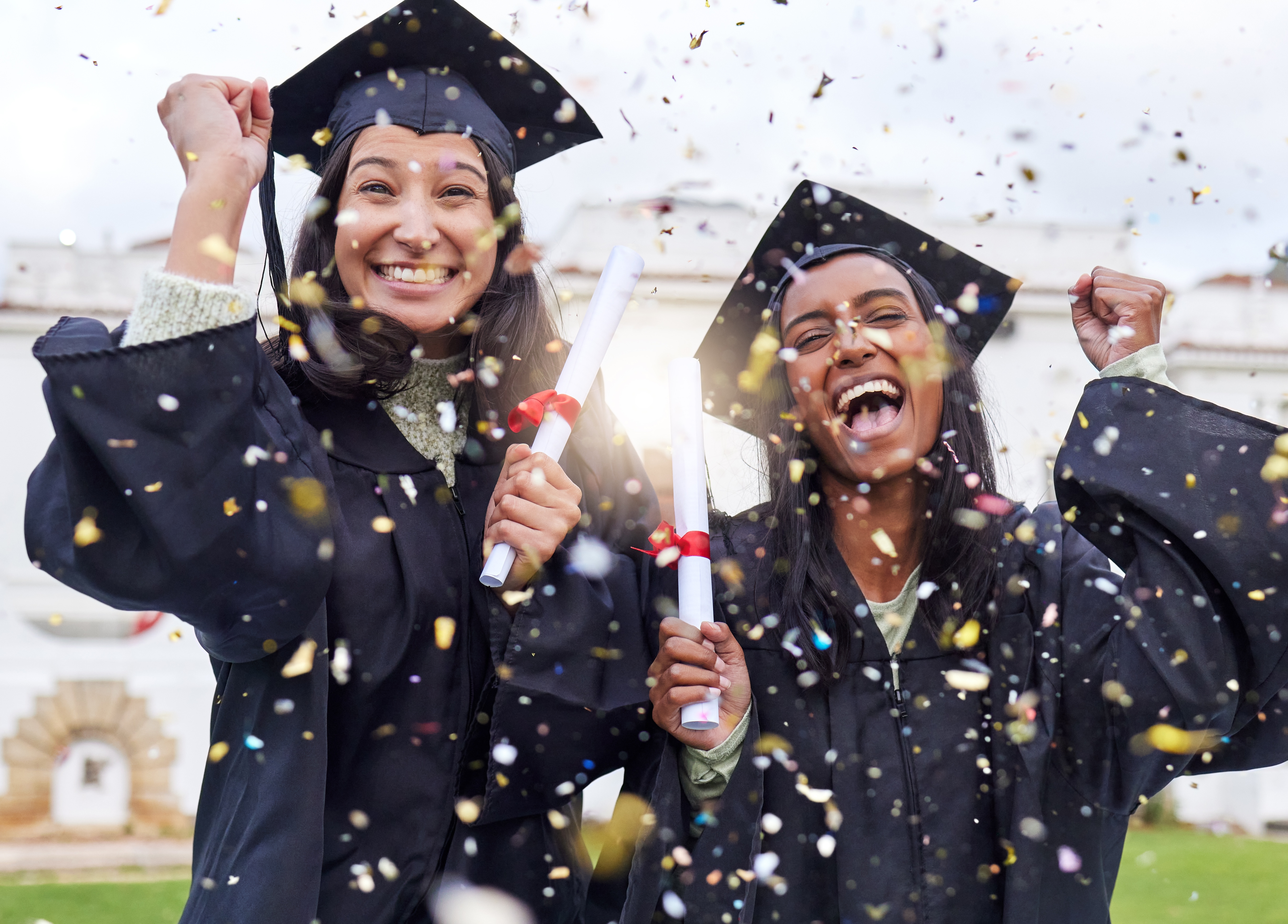 Two graduates in caps and gowns celebrate with diplomas amidst confetti, expressing joy and accomplishment