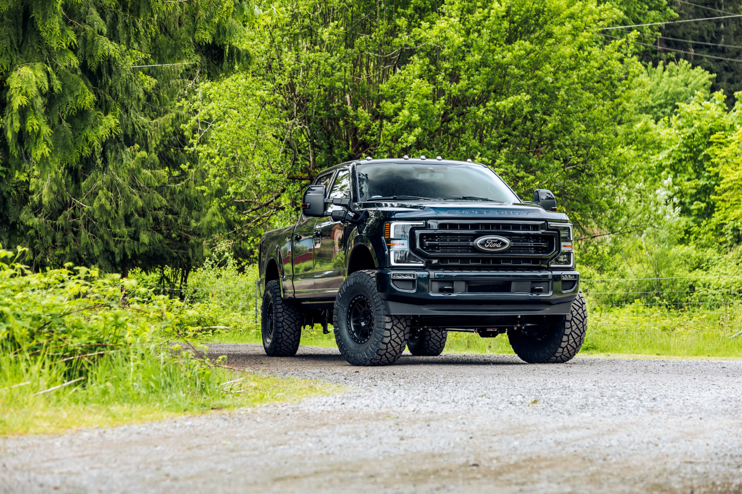 Large black pickup truck parked on a gravel path surrounded by lush greenery and trees