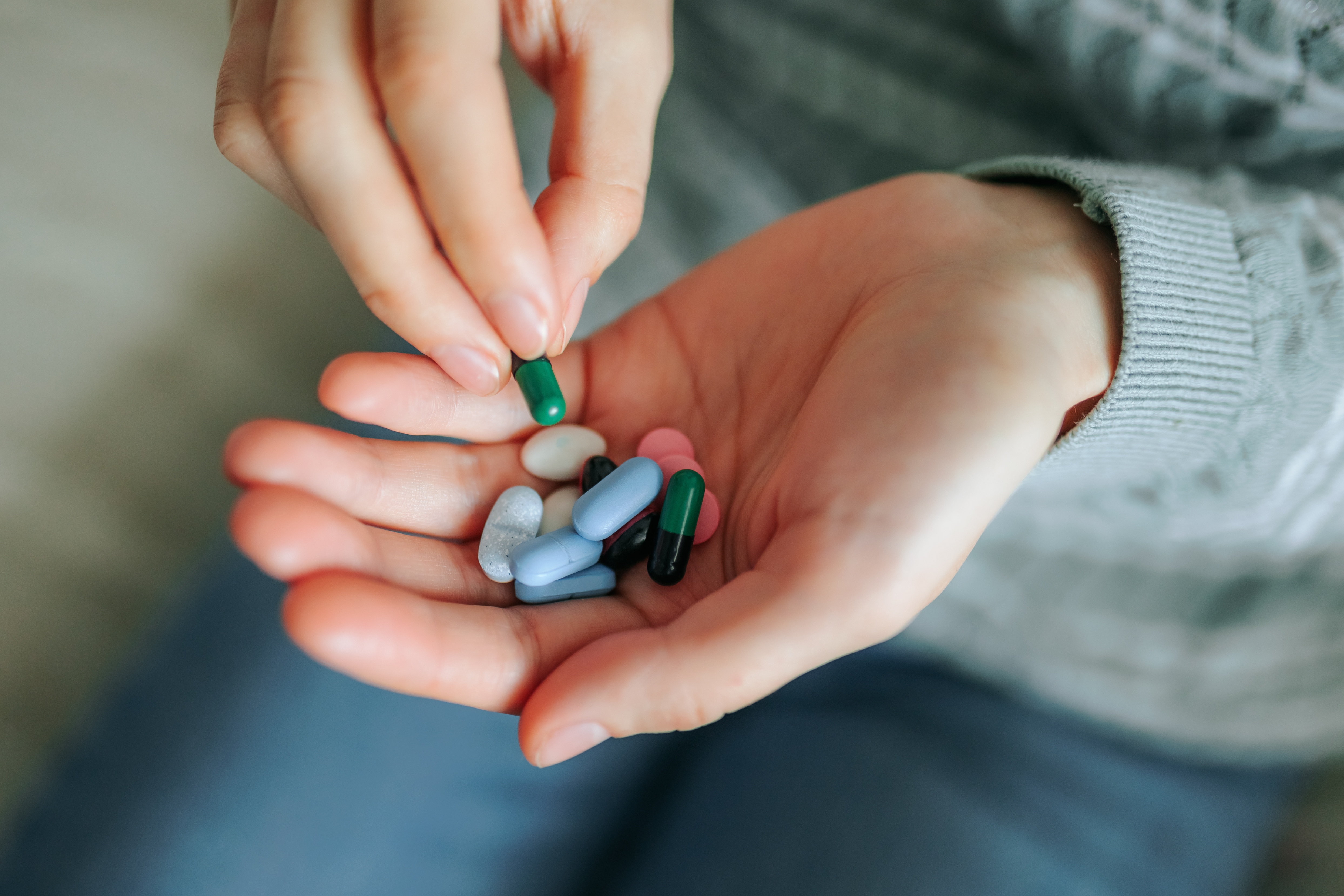 A person holds various pills in their hands, selecting one