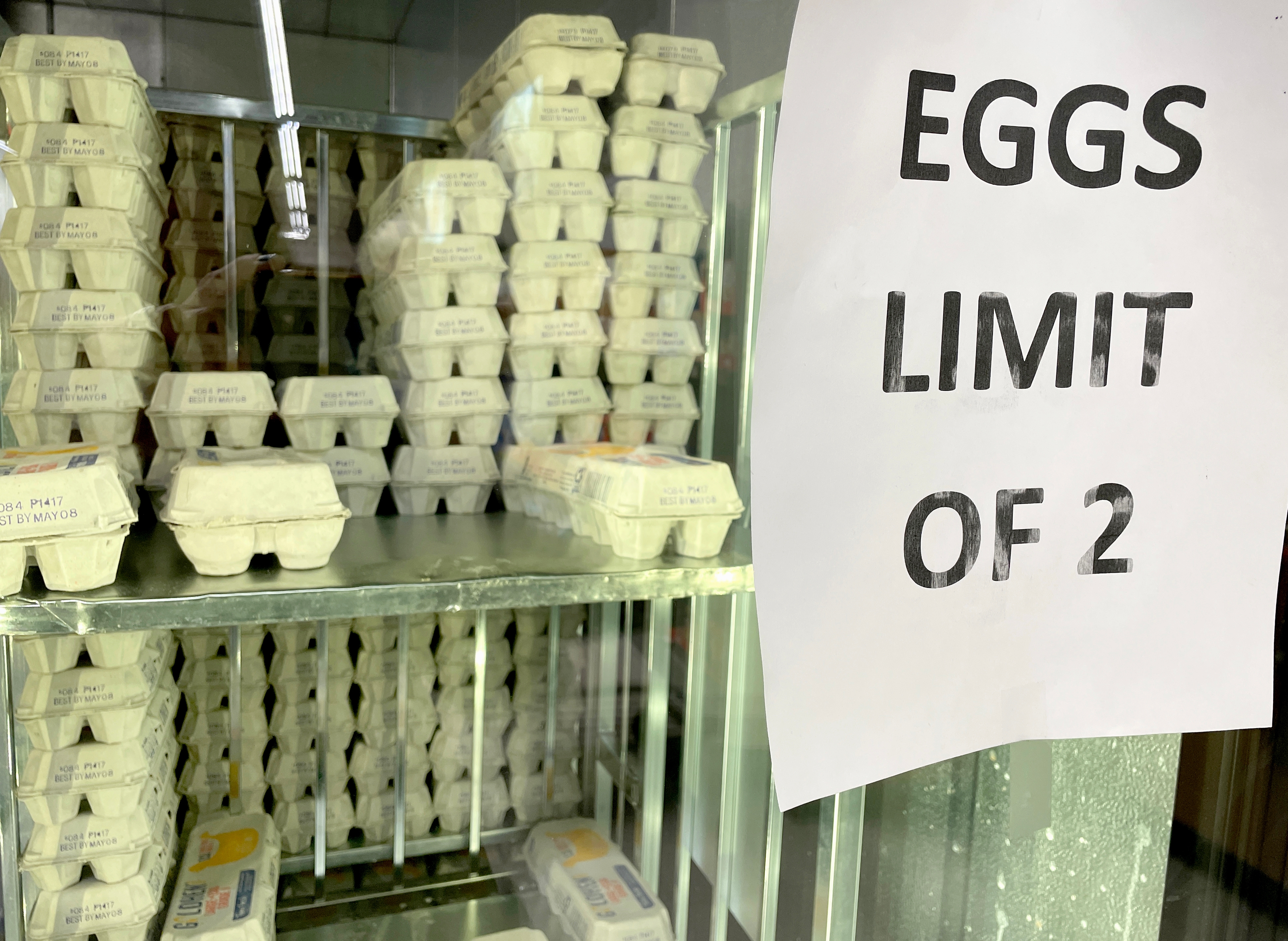 Egg cartons on display in a store fridge with a sign reading, "EGGS LIMIT OF 2," suggesting purchase restrictions