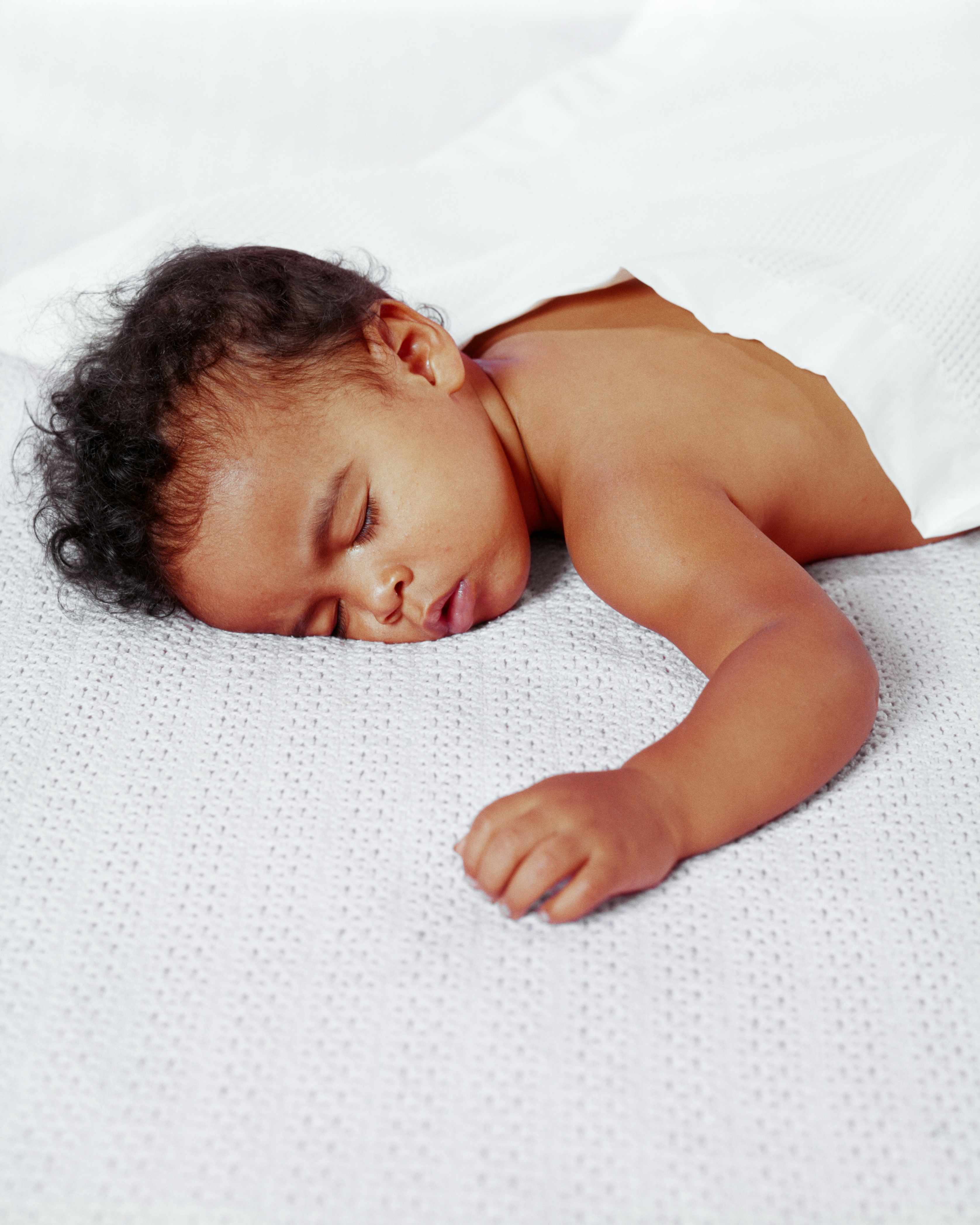 Baby peacefully sleeping on a textured surface, partially covered with a blanket