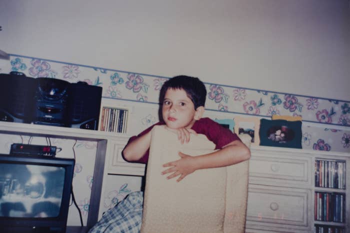 Young child leaning on a chair in a room with a stereo, TV, and decorative wallpaper
