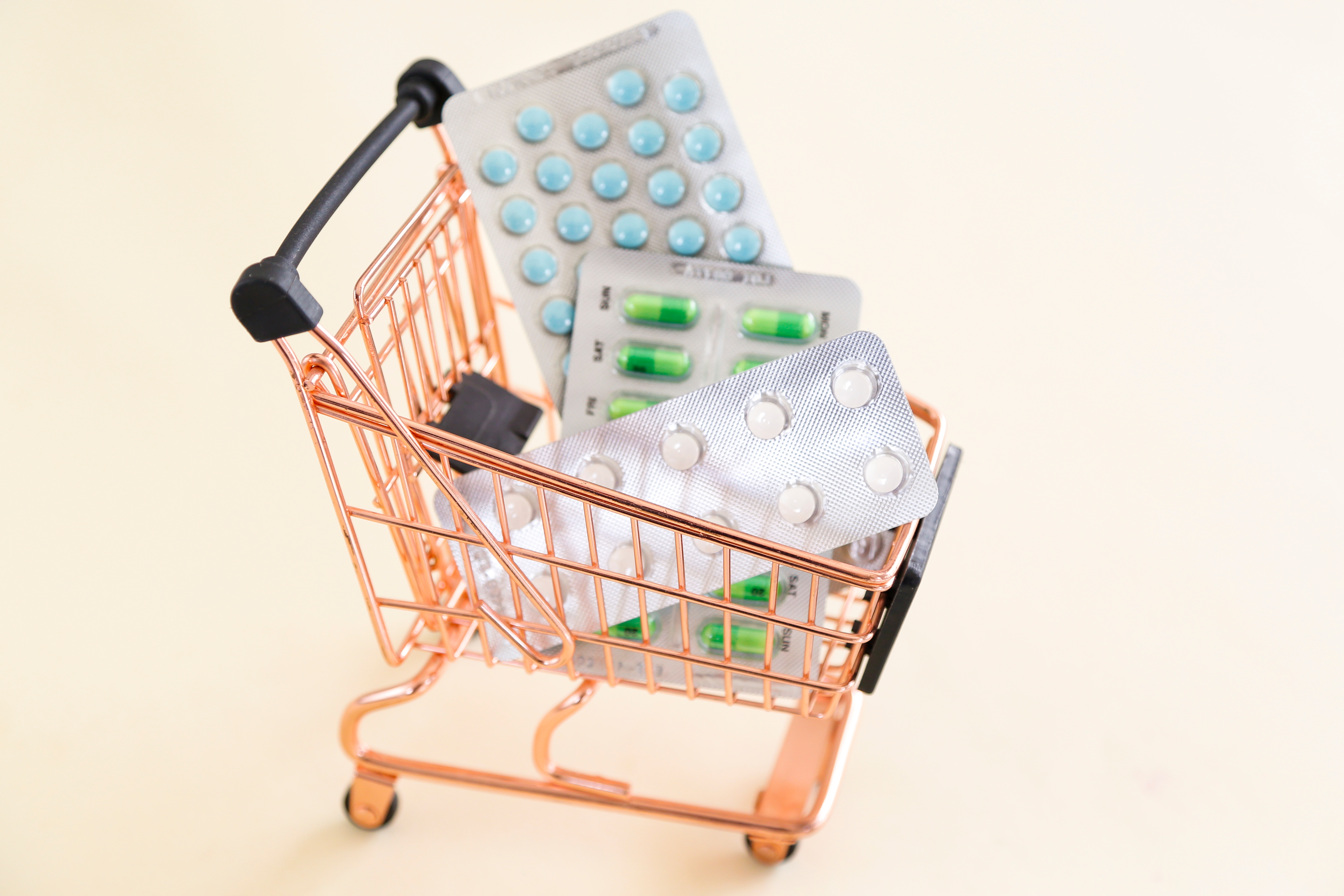 Mini shopping cart filled with blister packs of pills, symbolizing consumerism and healthcare