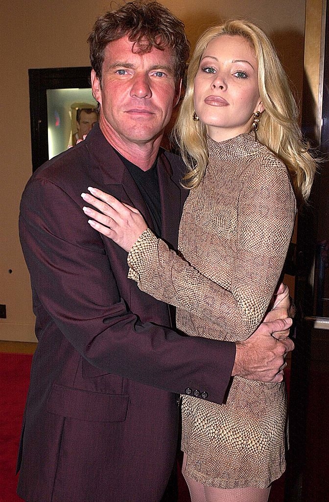 Two people embracing on a red carpet event; the man in a suit and the woman in a patterned dress