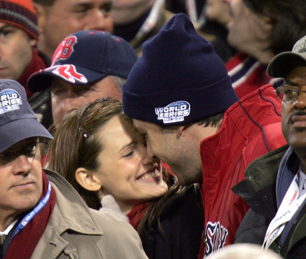 A couple shares a joyful, close moment at a sports event, surrounded by fans wearing baseball-themed attire