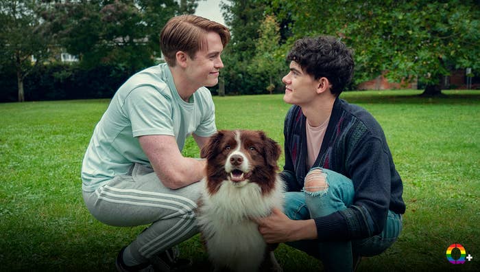 Dos personas agachadas en un parque, sonriendo mientras acarician a un perro