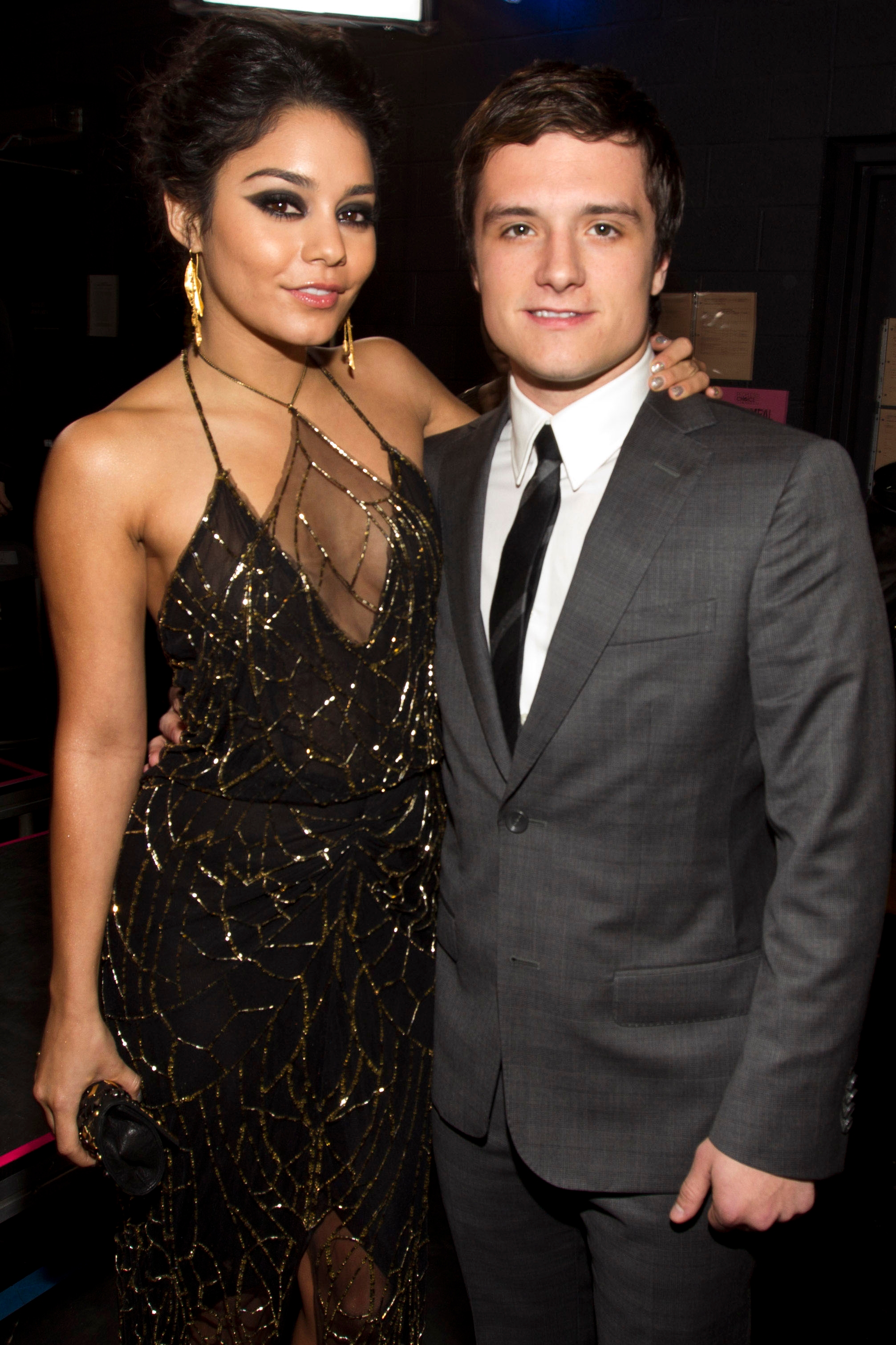 Two people smiling at an event. The person on the left wears a beaded gown; the person on the right wears a suit and tie