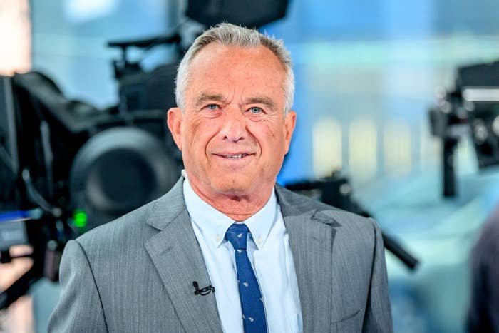 A person in a suit and tie is standing in a studio environment with cameras in the background