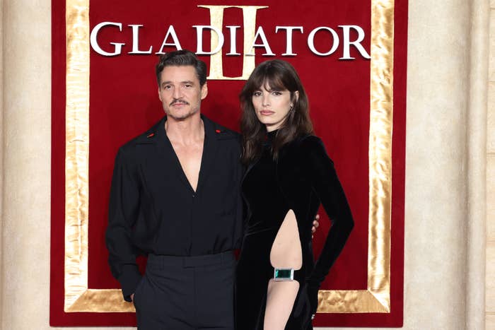 Two individuals on a red carpet for a &quot;Gladiator II&quot; event. One wears a black shirt; the other in a sleek black dress with a cut-out