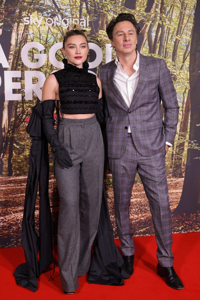 Two celebrities pose on the red carpet. One wears a black crop top and checkered pants; the other wears a plaid suit