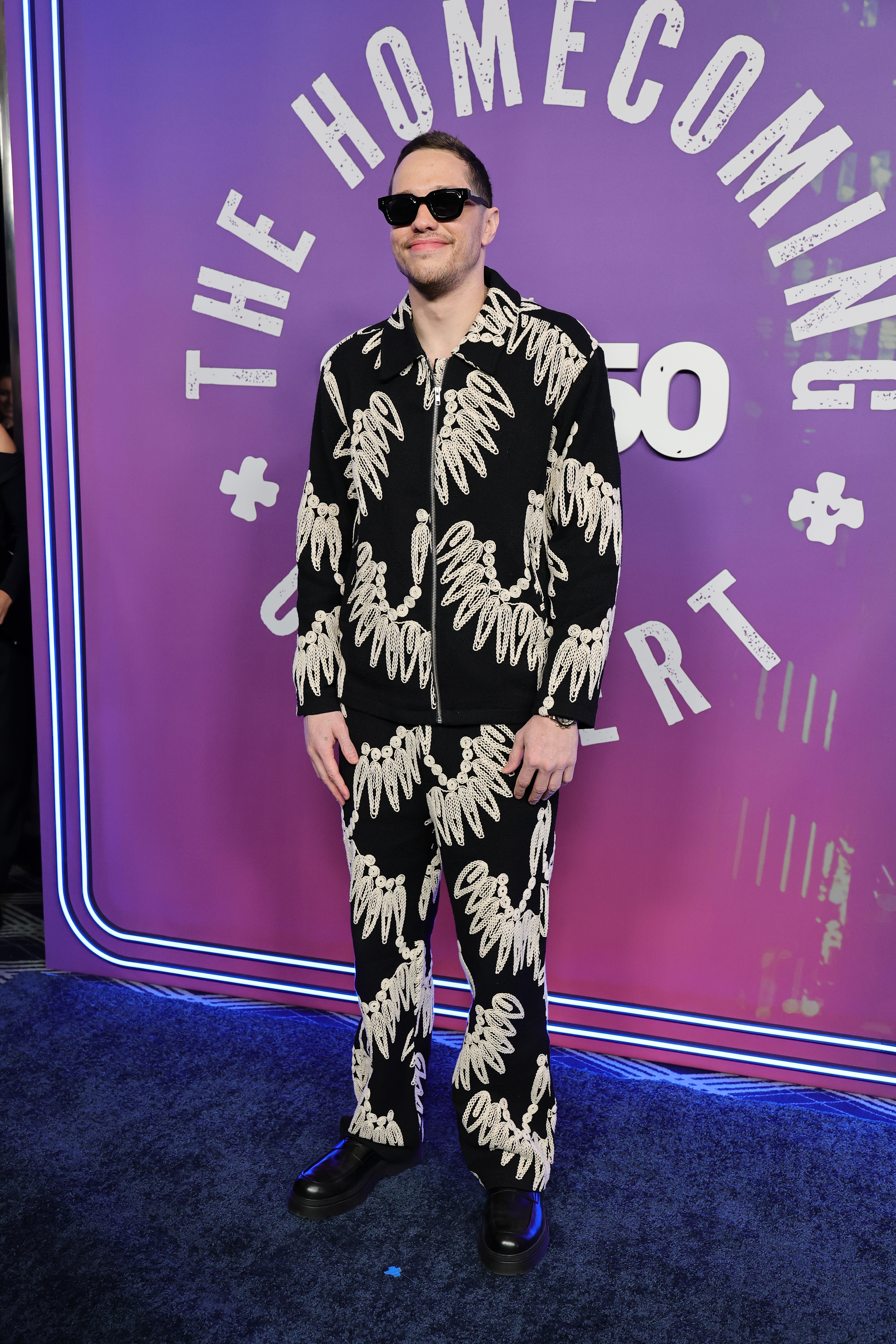 Person in a patterned suit and sunglasses on a blue carpet at a celebrity event
