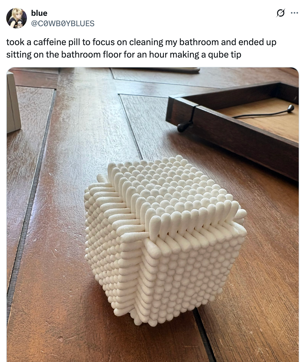 A cube made of stacked cotton swabs sits on a wooden floor