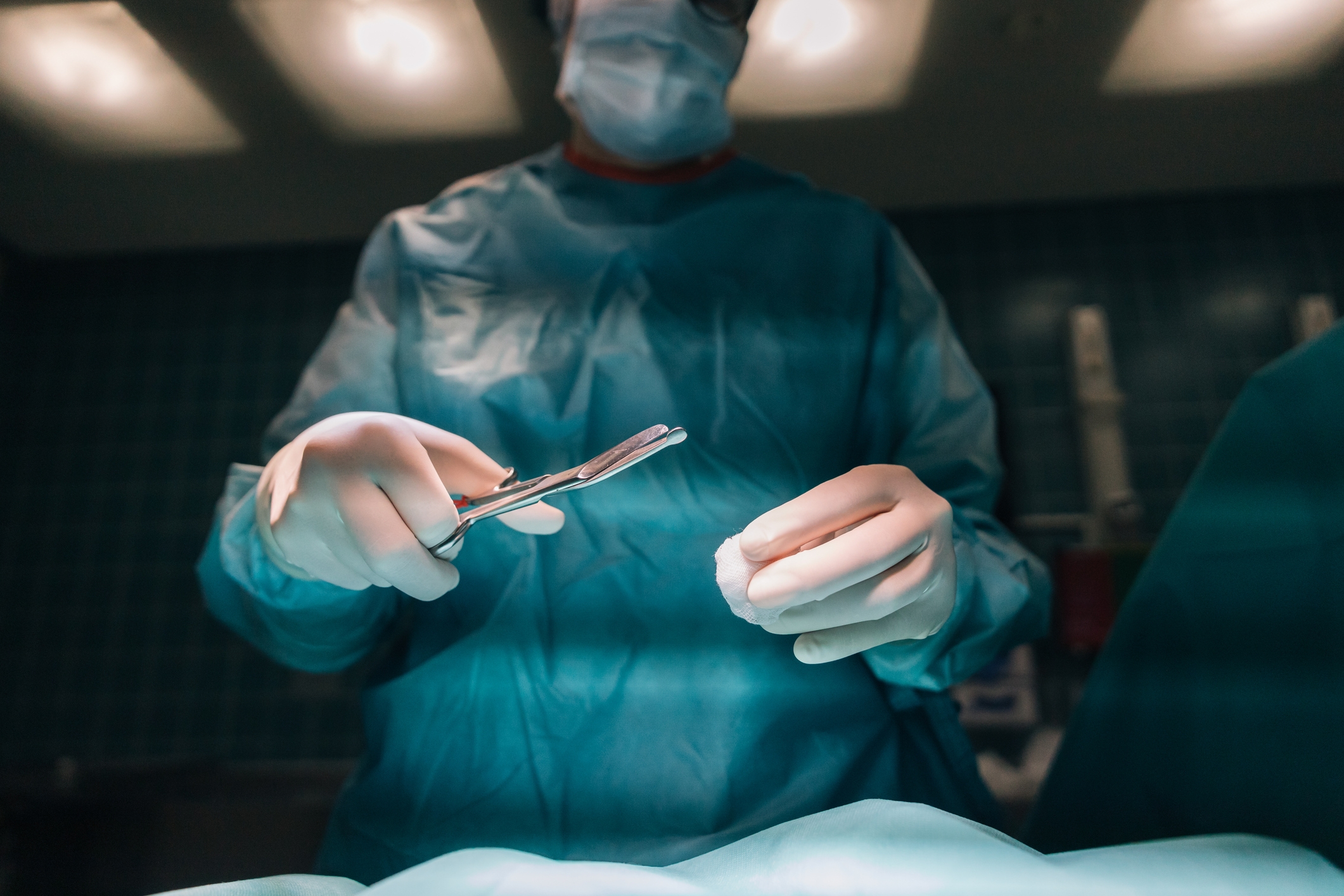Surgeon in scrubs and mask confidently holding surgical tools, preparing for a medical procedure in an operating room