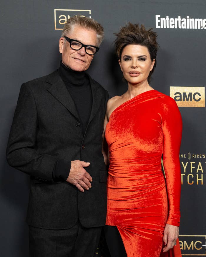 Harry Hamlin in a suit with glasses and Lisa Rinna in a red velvet, one-shoulder dress pose at a media event