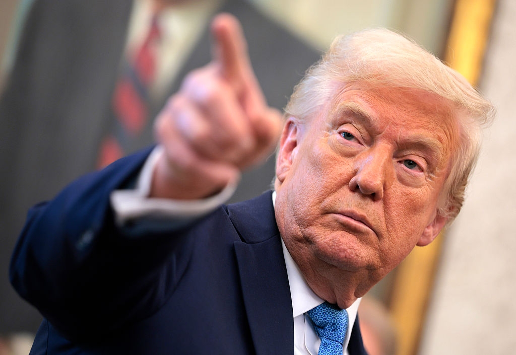 A person in a suit points with a serious expression in a formal setting