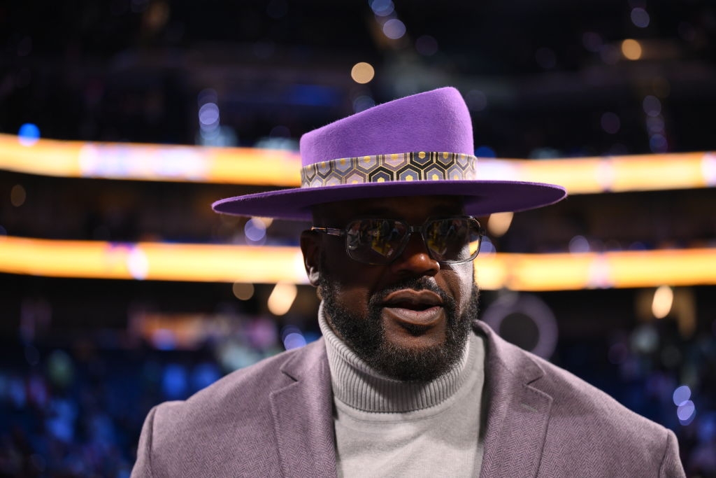 A person wearing a stylish wide-brimmed hat, sunglasses, and a turtleneck on a special event carpet