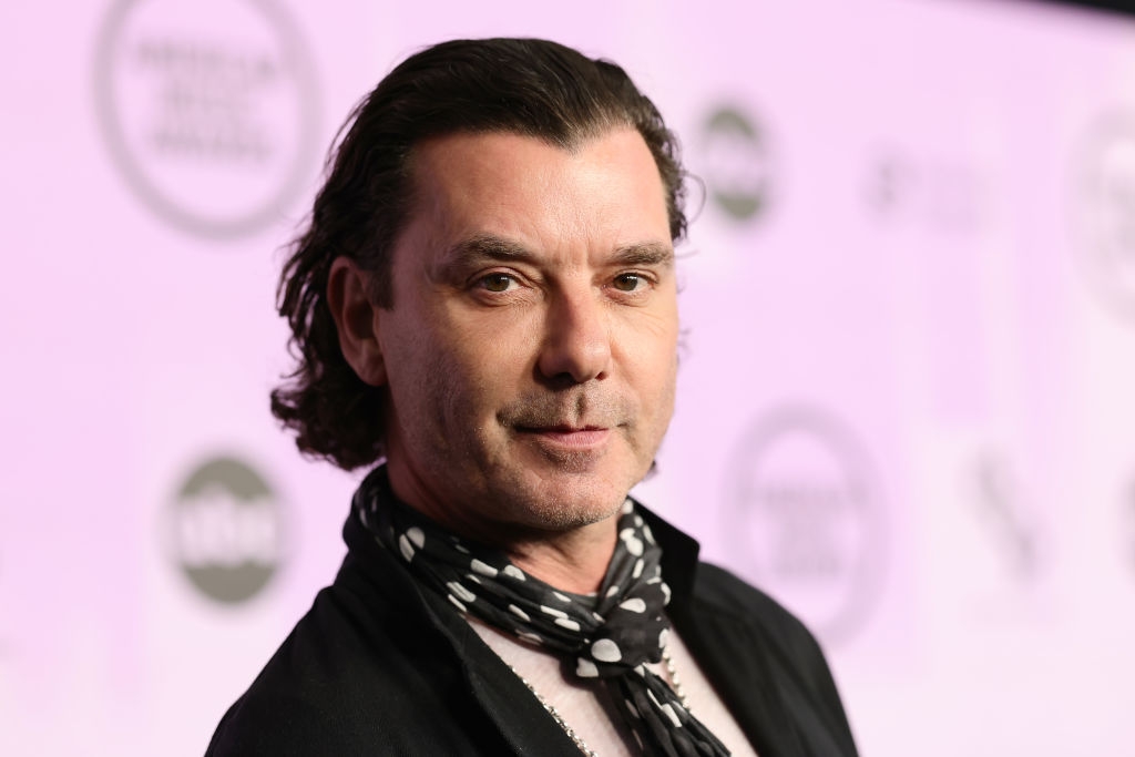 Person on a red carpet wearing a polka dot scarf and dark jacket with a neutral expression