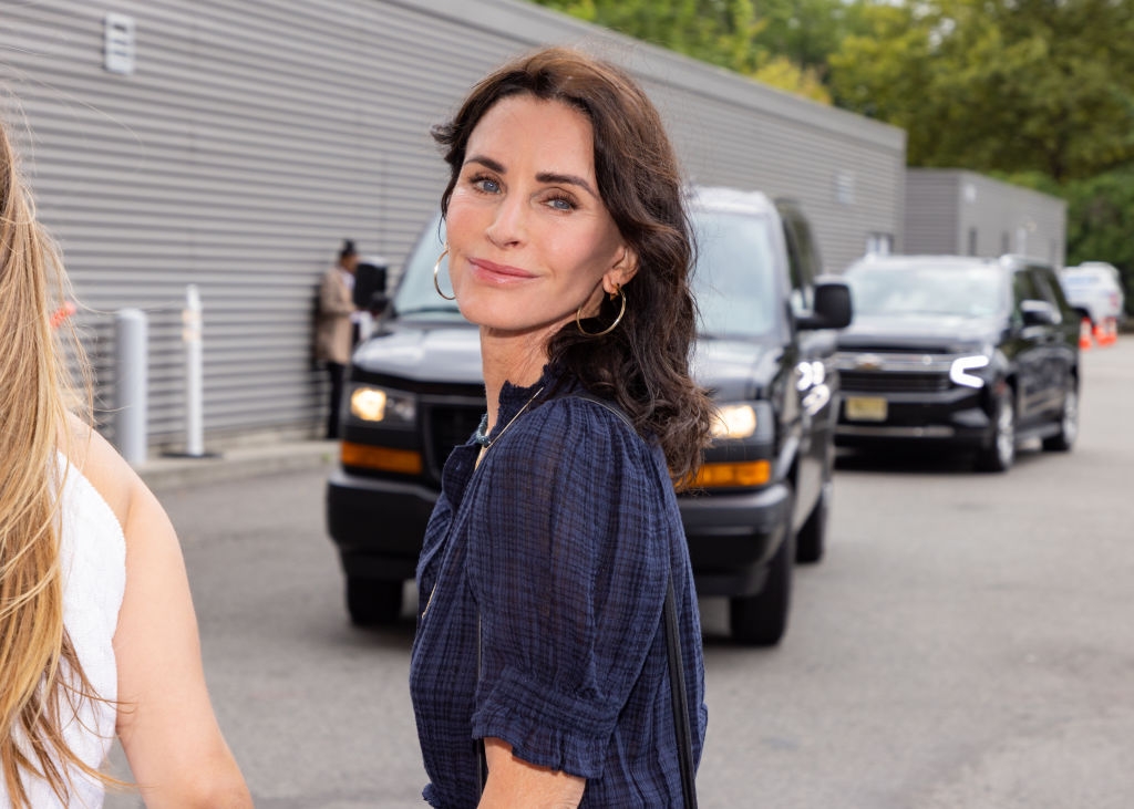 Person with shoulder-length dark hair poses outdoors in a casual setting, wearing a blue dress