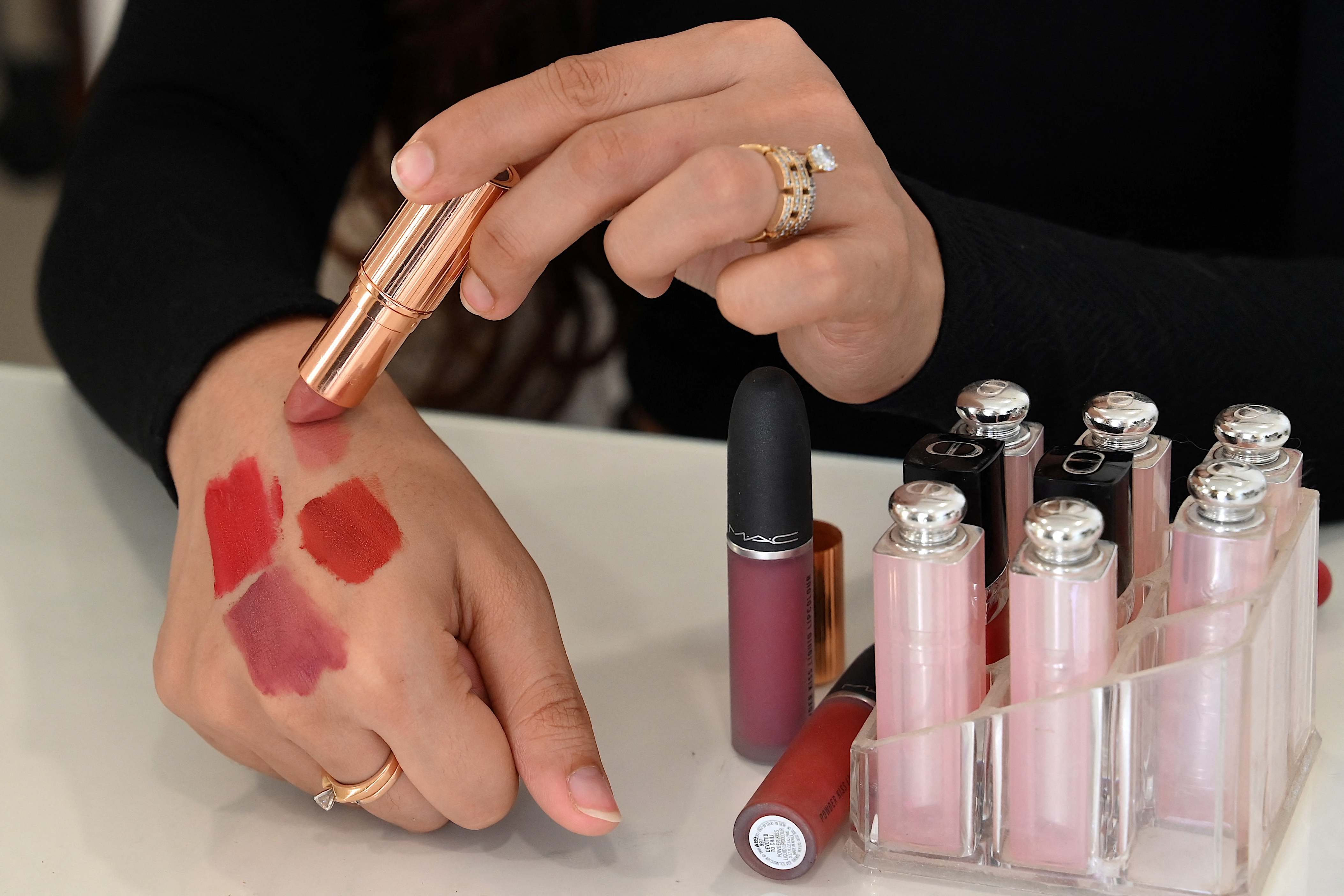 Person testing various lipstick shades on their hand, with several lipsticks displayed on a nearby surface