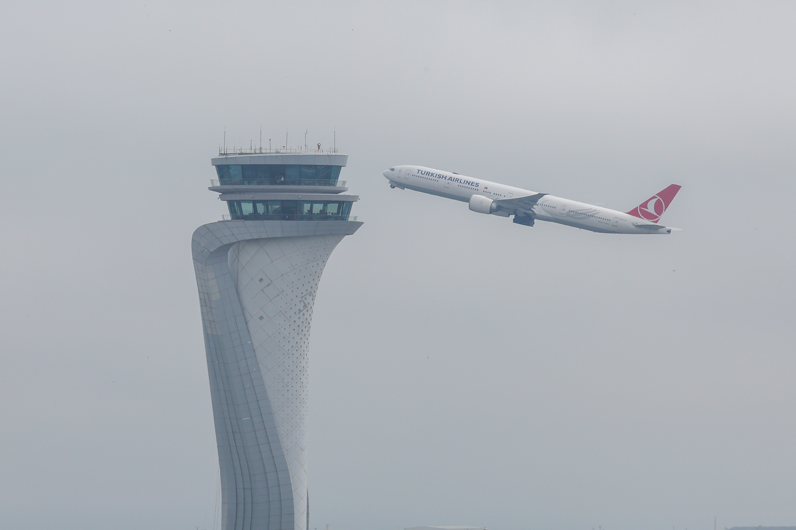 Airplane taking off near a uniquely designed air traffic control tower against a cloudy sky