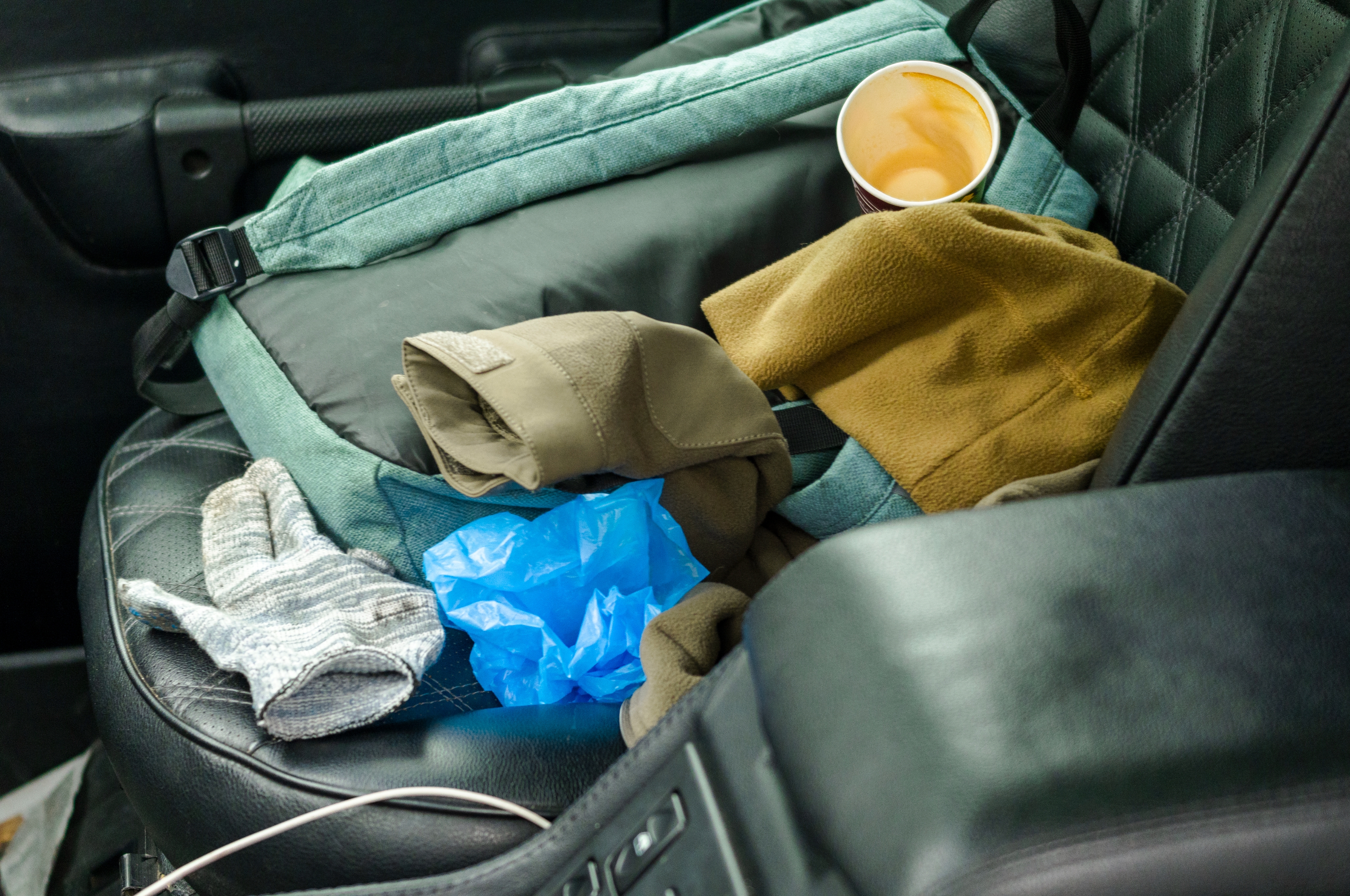 Car seat with a backpack, disposable cup, sweater, gloves, and plastic bag scattered on it