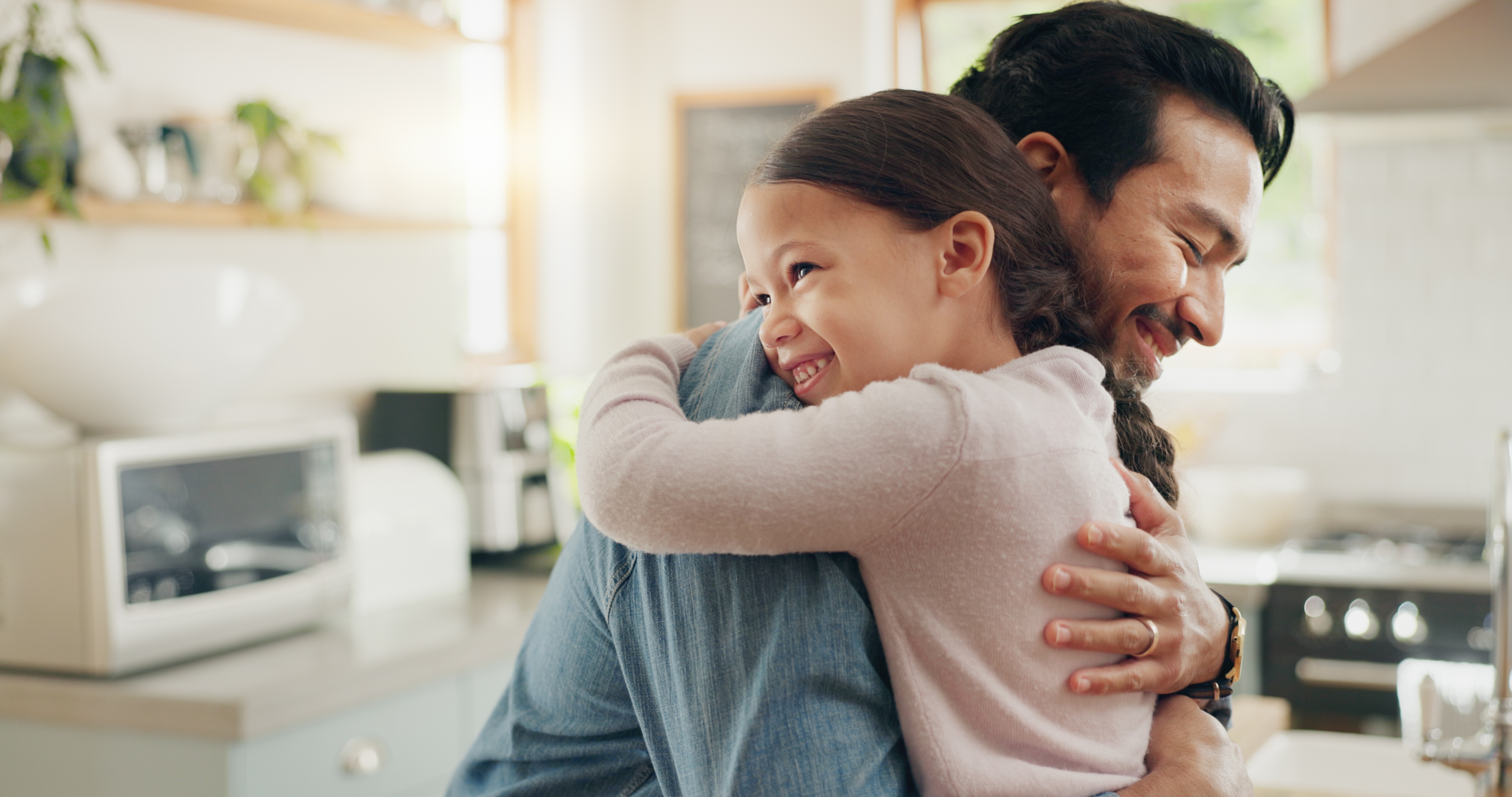A man and a young girl share a joyful hug in a cozy kitchen setting, smiling warmly